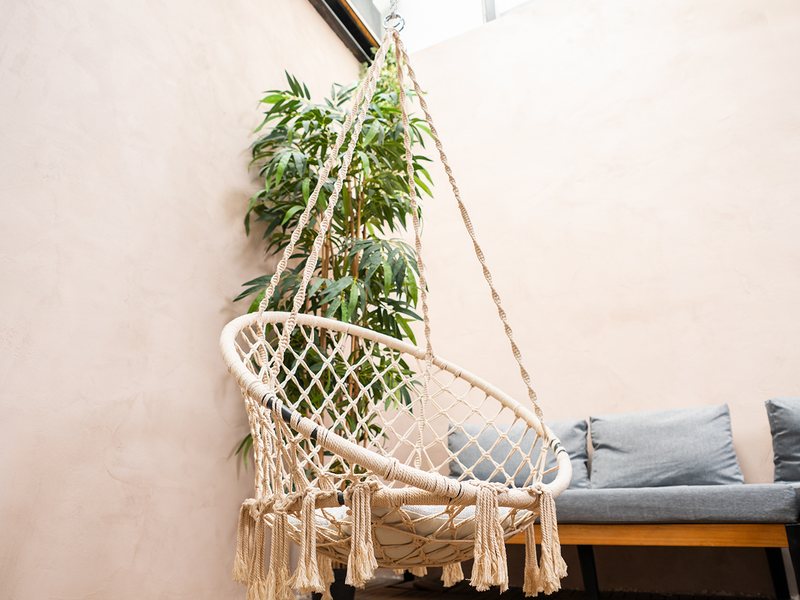 Le coin détente du Studio Urban : fauteuil suspendu en macramé, plantes et banquette sur la terrasse en bois.