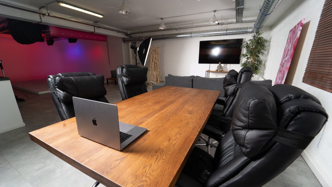 La table de réunion en chêne du Studio Urban, le canapé et la TV grand écran pour le visionnage, avec le cyclorama éclairé en fond.