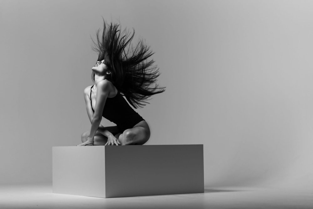 Photo de danse en noir et blanc réalisée au Studio Urban : mouvement de cheveux sur un cube blanc, fond de cyclorama dégradé.